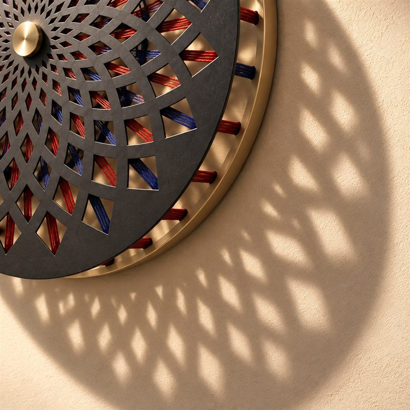 Parallax Medallion from below, its perforations and cords throwing a field of light and shadow across the wall